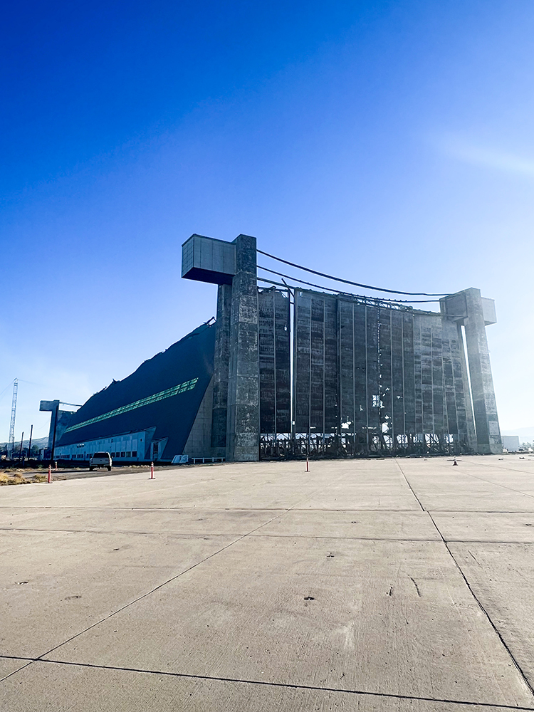 Large, partially-demolished concrete hangar under a clear blue sky.