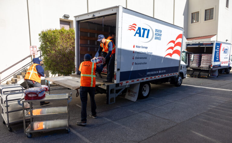 Workers in orange safety vests unloading supplies from ATI Disaster Recovery Services trucks.