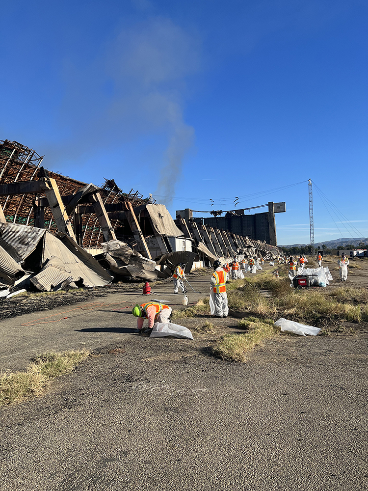 Workers in protective suits clean up debris from a collapsed building.