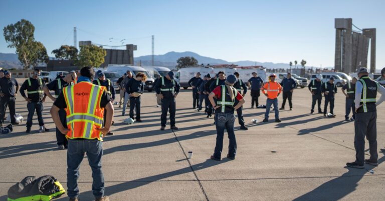 A group of people in safety vests participate in a safety training or meeting in a large parking lot.