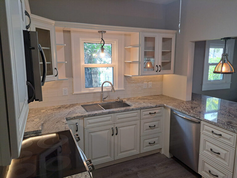 A bright, remodeled kitchen with white cabinets, granite countertops, and stainless steel appliances.