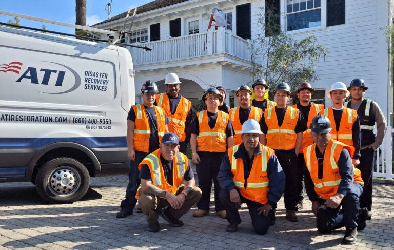 Group photo of ATI Disaster Recovery Services employees in orange safety vests and hard hats in front of their company van.