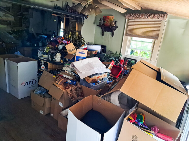 A room filled with numerous cardboard boxes overflowing with various items, indicating a cluttered or in-progress move.