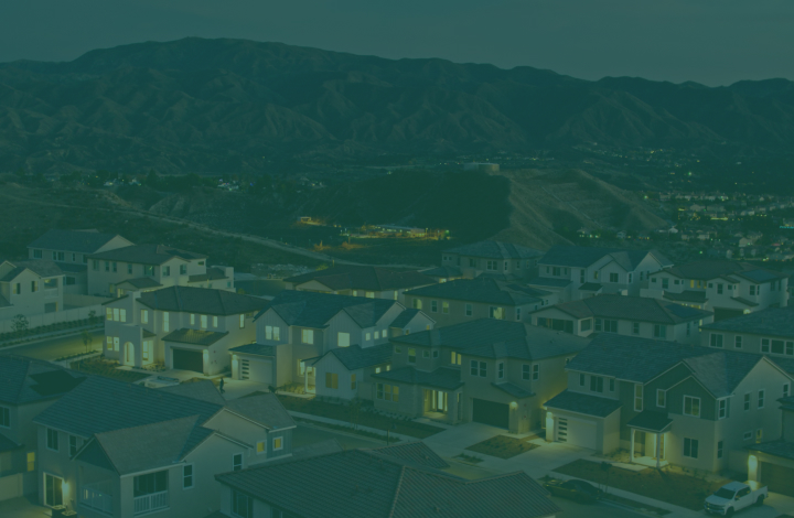 Aerial view of a residential neighborhood at night, nestled in a valley with mountains in the background.