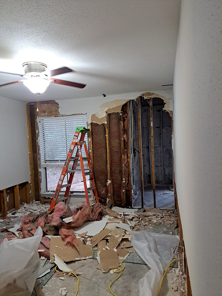 Room under renovation with drywall removed, debris on the floor, and a ladder.