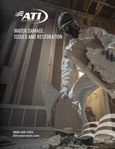 A worker in protective gear removes water-damaged drywall.